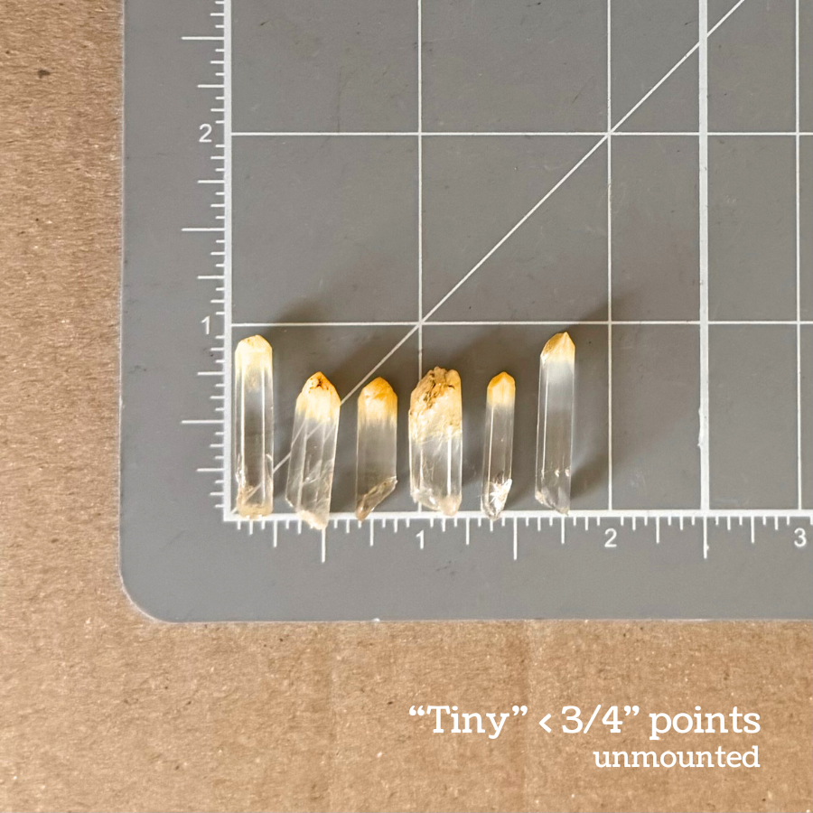 Titled as the tiny size, points under three quarters of an inch in length, and unmounted. Six of the points are spread on a measuring mat for scale, ranging from just under an inch in length to closer to half an inch.