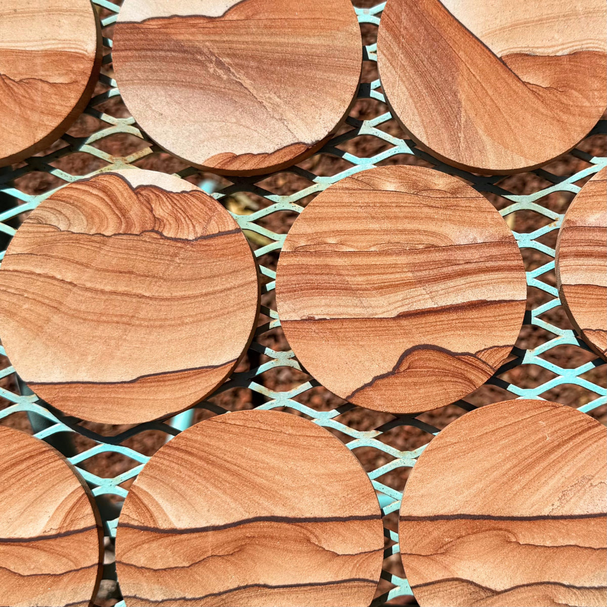 Round flat red sandstone coasters spread evenly over a table-top with similarly colored gravel beneath them.