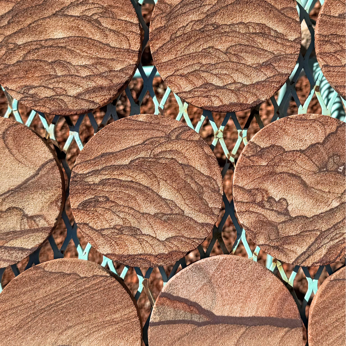 Round flat reddish-brown sandstone coasters spread evenly over a table-top with similarly colored gravel beneath them.
