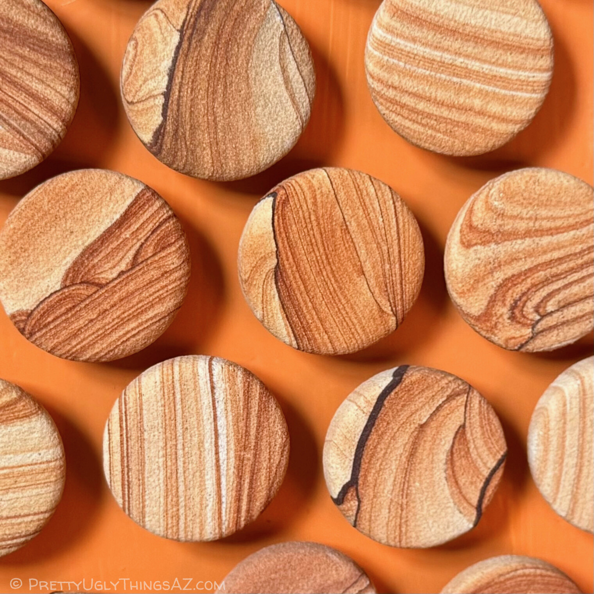 Several sandstone magnets evenly places on an orange background. The magnets are flat round discs of a red-tinged picture sandstone.