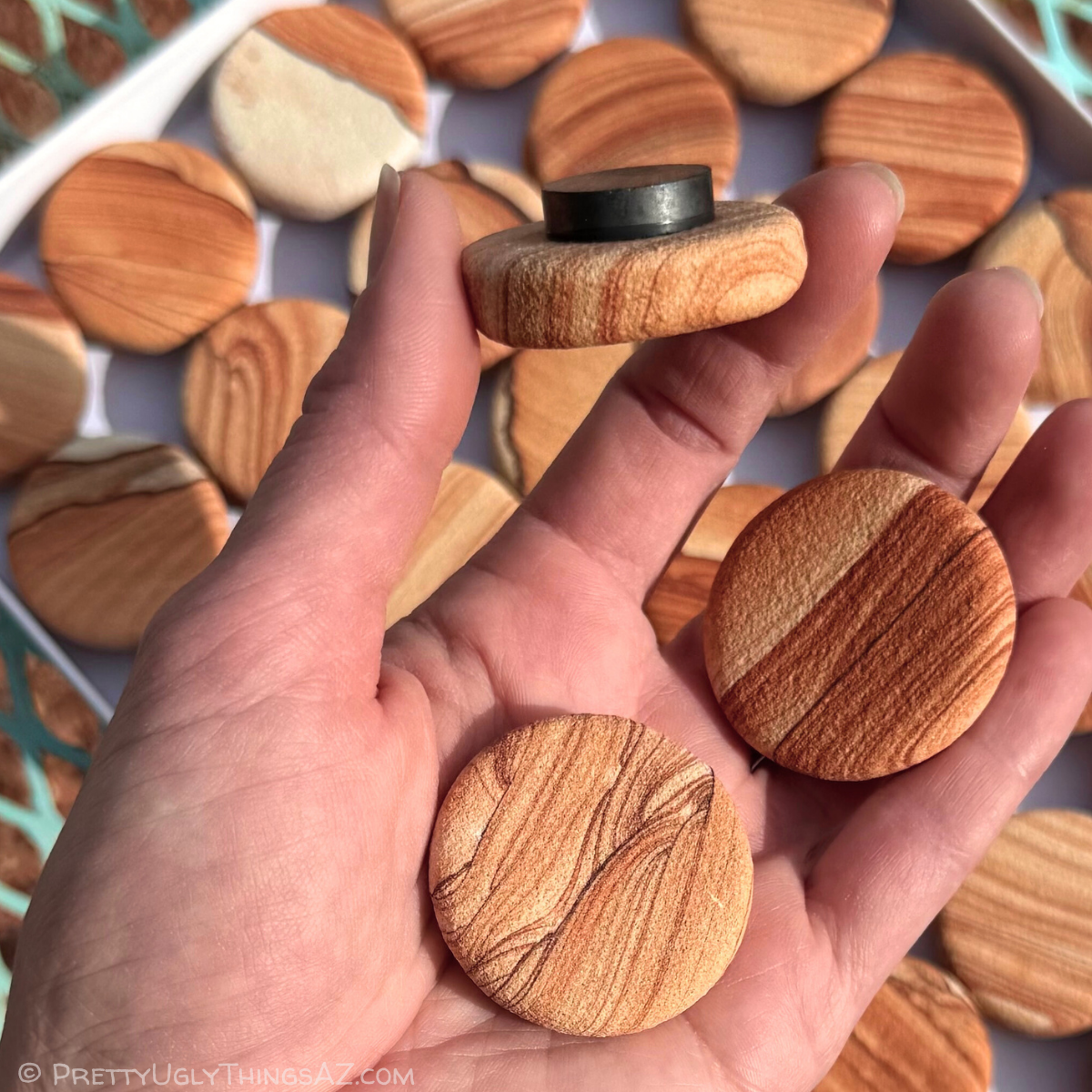 Two magnets held in a palm to show scale, with a third flipped sideways to show the magnet is thick.