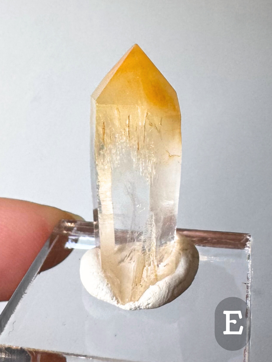 Option E, a small well-proportioned point with the top third a saturated orange-yellow color, the bottoms of the gold fibers catching reflections as the material transitions to clear and colorless.