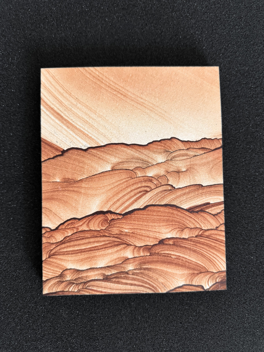 A more distant view of the full piece on a black background, the sky a light orange cream color, and the hills a saturated red-brown pattern.