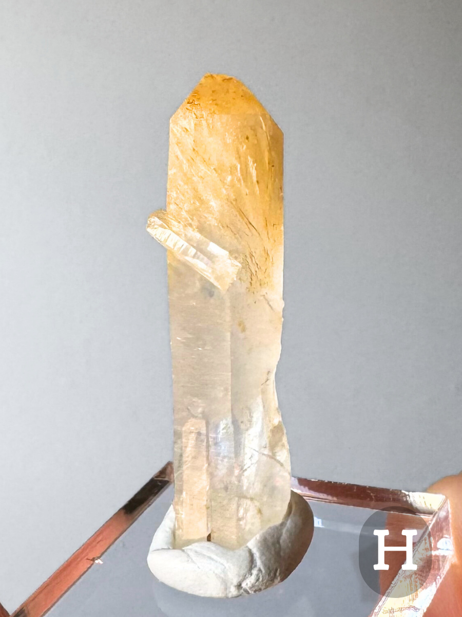 Option H, a long narrow point with a small quartz point attached diagonally on the surface. The top third of the point is included with fibrous orange-yellow halloysite, with the rest a slightly milky colorless quartz.