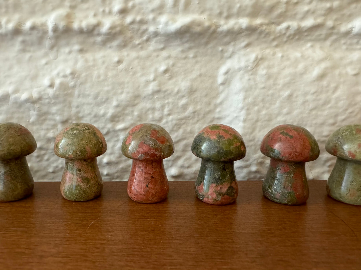 A row of unakite mushrooms showing some deeper salmon colored spots and darker green variations
