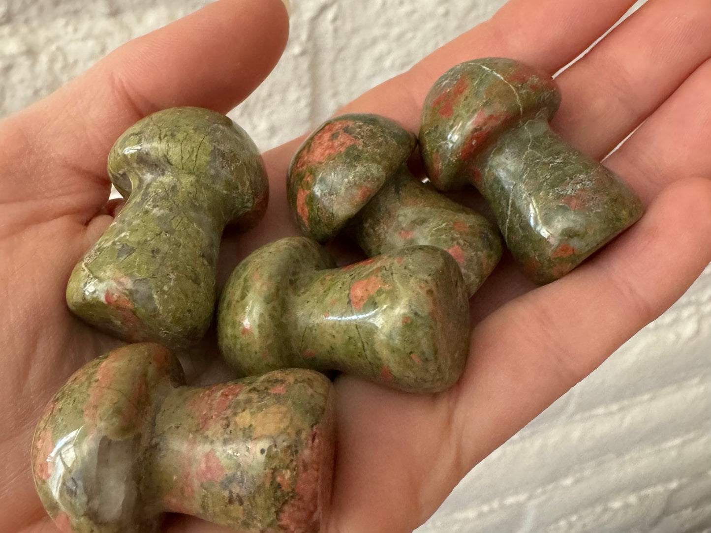 A hand holding five unakite mushrooms to illustrate scale
