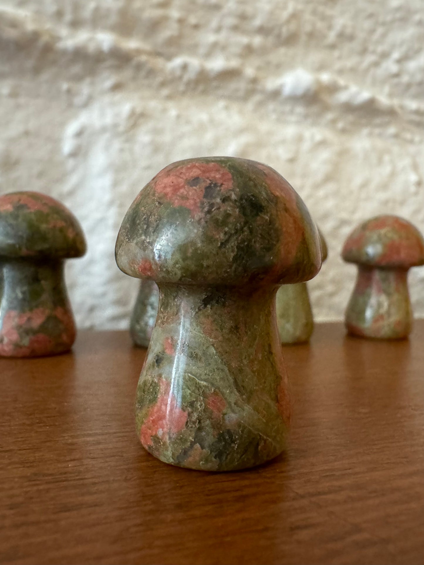 Example variant of a unakite mushroom, dark green color with medium pink spots and a quartz vein winding through. There are more variants in the background.