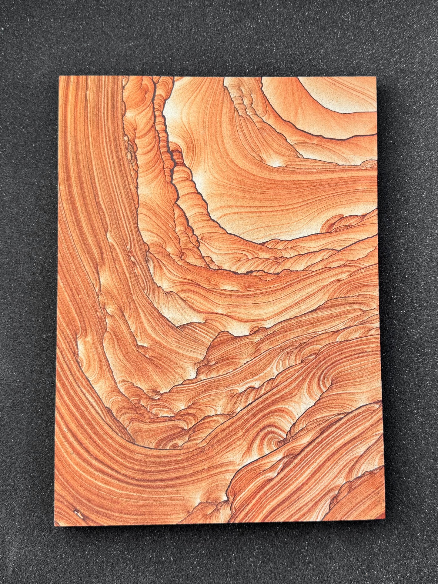 A large rectangular slab of sandstone, a bit smaller than a standard piece of printer paper, oriented in portrait. The sandstone has good red-orange coloration and excellent pattern. Thin dark iron bands curve across the surface with looping and scallop-like edges, and curving sandstone layering between them. Pattern is lighter colored and less complex in the upper right, with layers curving from the upper left to the right side around this. It vaguely resembles looking out of a cave, light in the distance