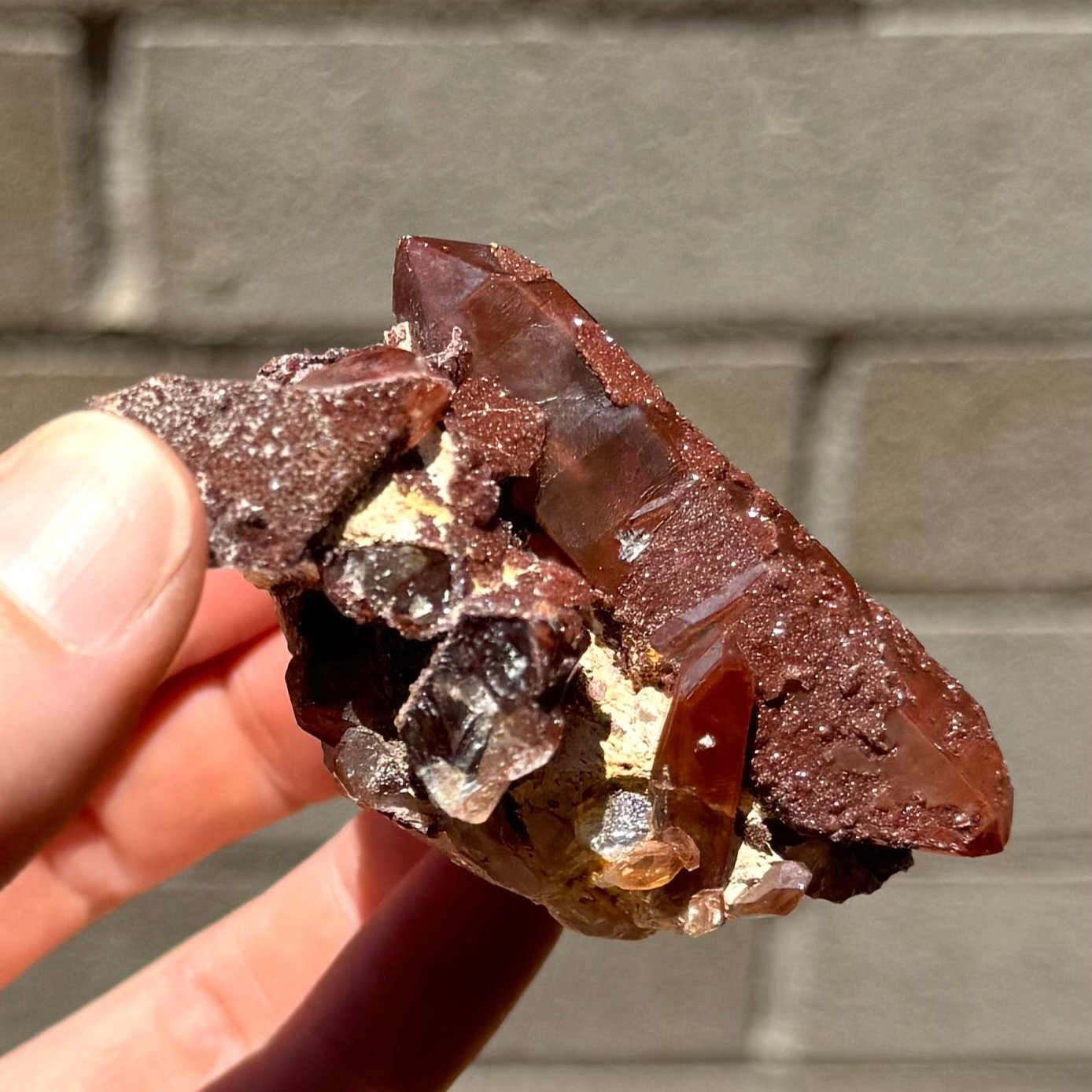 Side-view of the specimen, with a poor surface luster of the red quartz interruped by glittering druzy. Near the base, there is a well-formed small point with phantom coloring