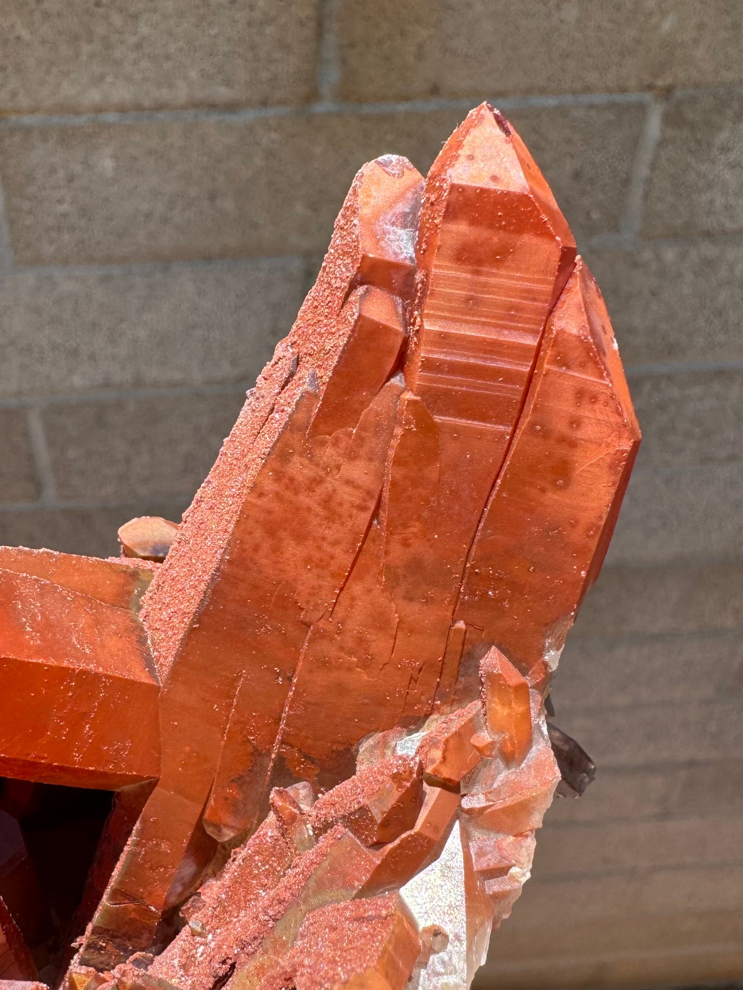 Detail of the largest crystal cluster, three parallel points forming a wide flat crystal. The surface is a dull red brown, with darker spots.