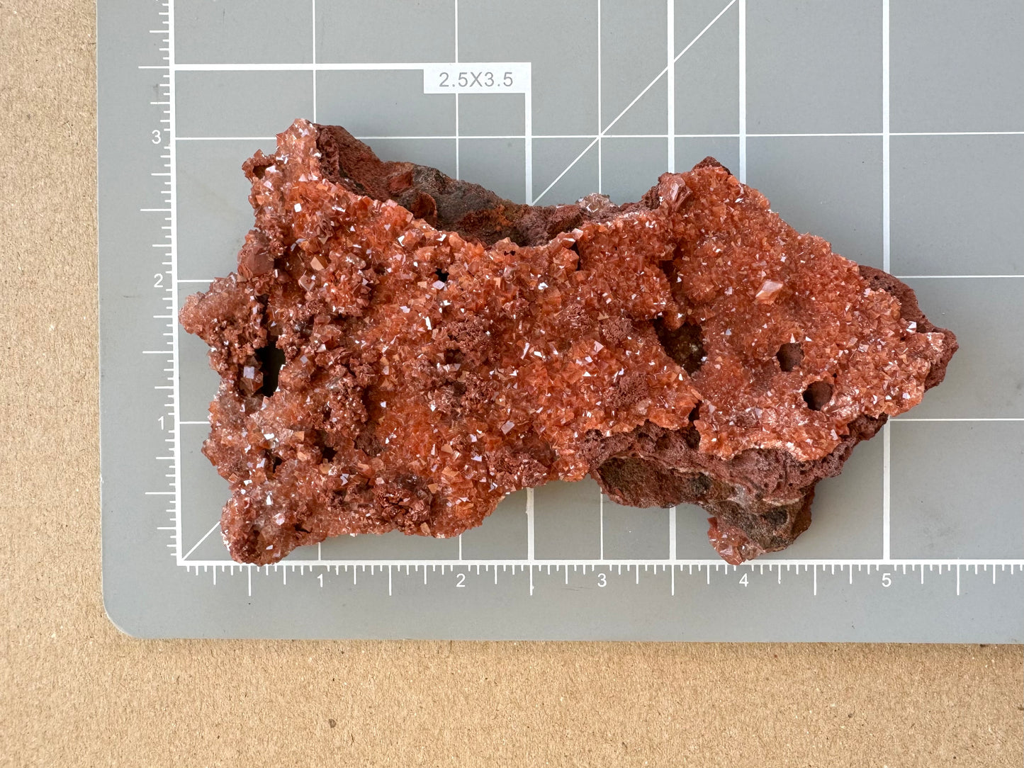 The mineral on a measuring mat, showing it is about five by two and a half inches, three inches at the widest.