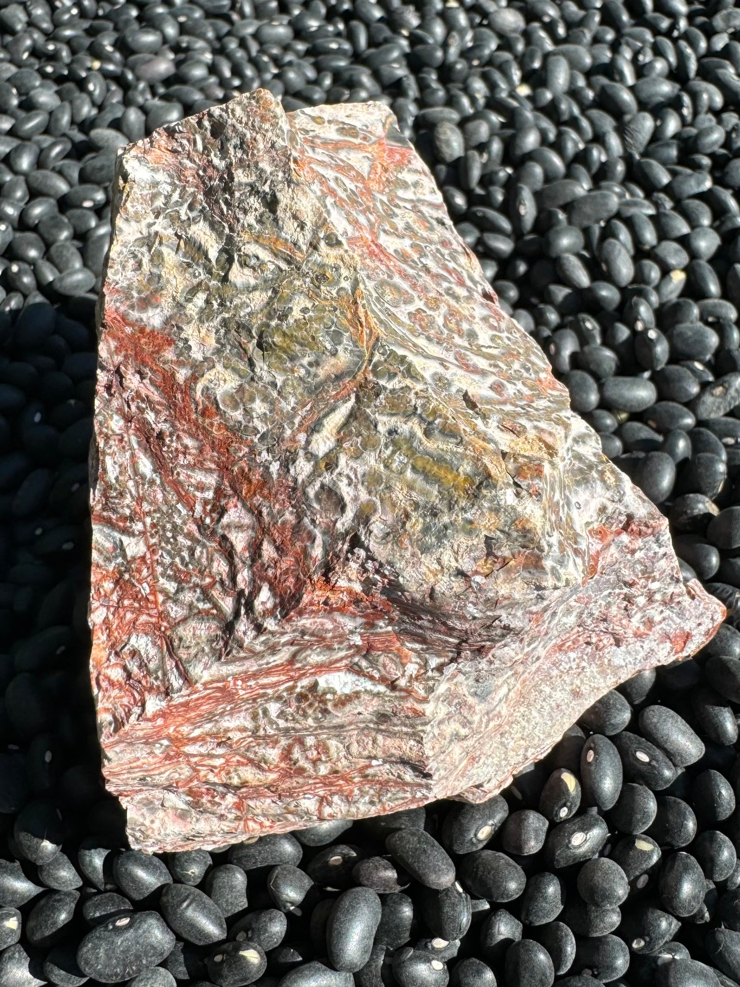 A different side of the piece with spidery thin red veins crossing one corner, ending at a thick red stripe. On the other side of the stripe the pattern changes to elongated yellow-and-gray spherulites, which deepen in color to red on the other side.