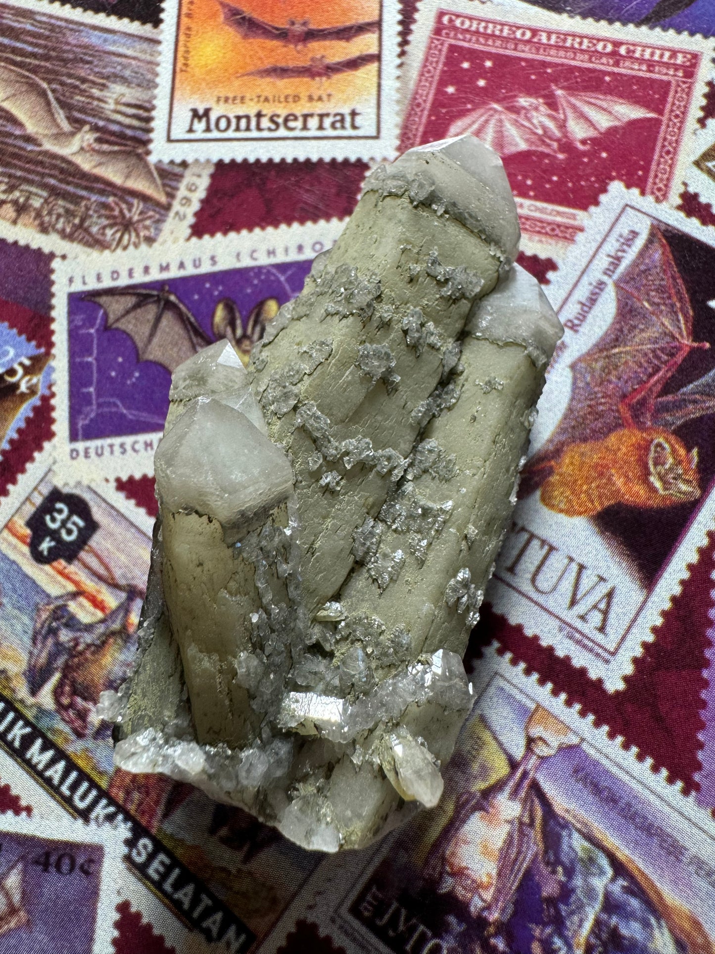 A closer view of the cluster with light shining at it, showing most of the surface is a matte off-tan color. One well formed small quartz crystal reflects near the base.