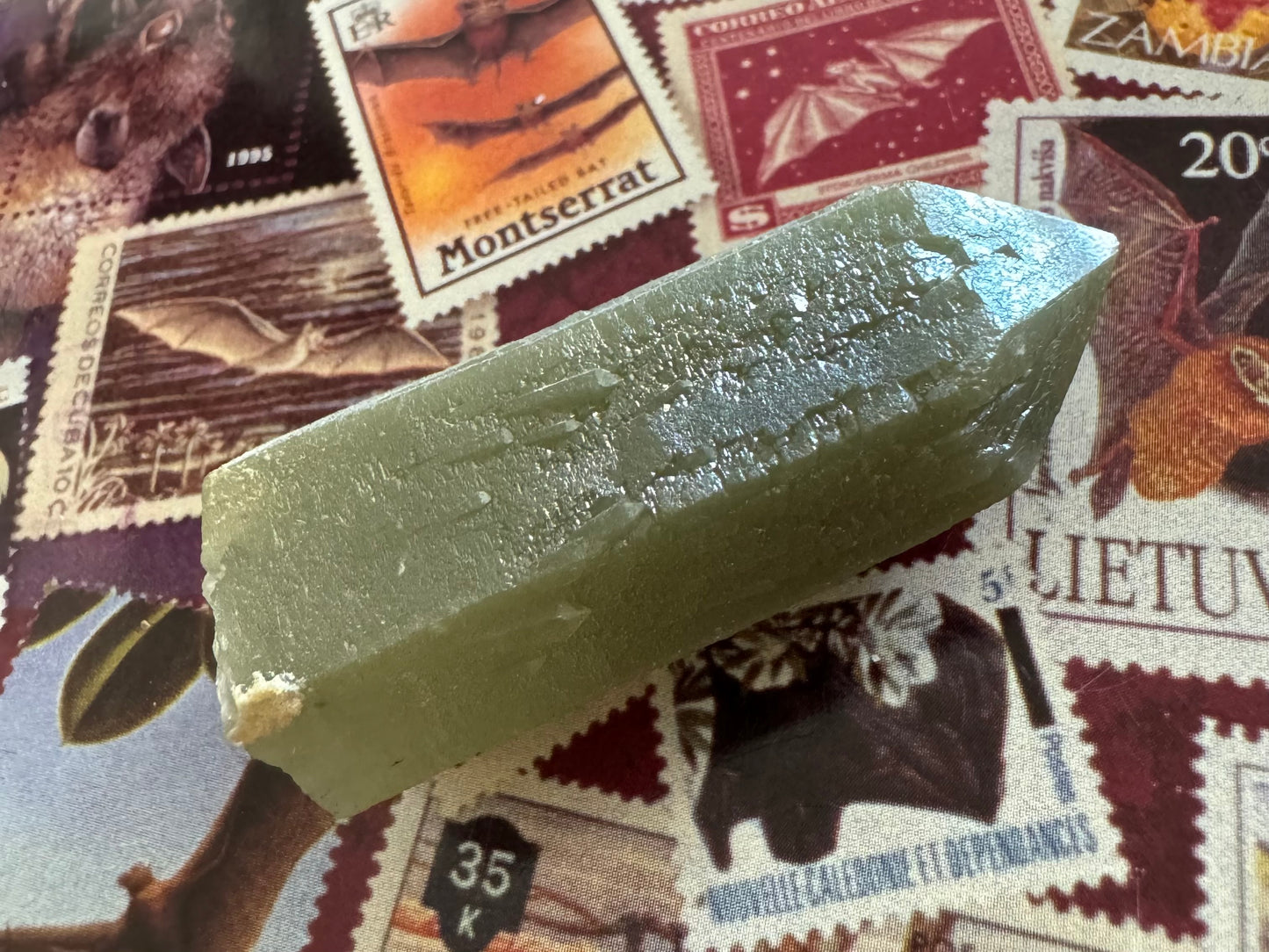 The point tilted into the light so the surfaces reflect, highlighting the complex surface patterning caused by the sprouting growth. There is a patch of an opaque white mineral on a corner of the base.