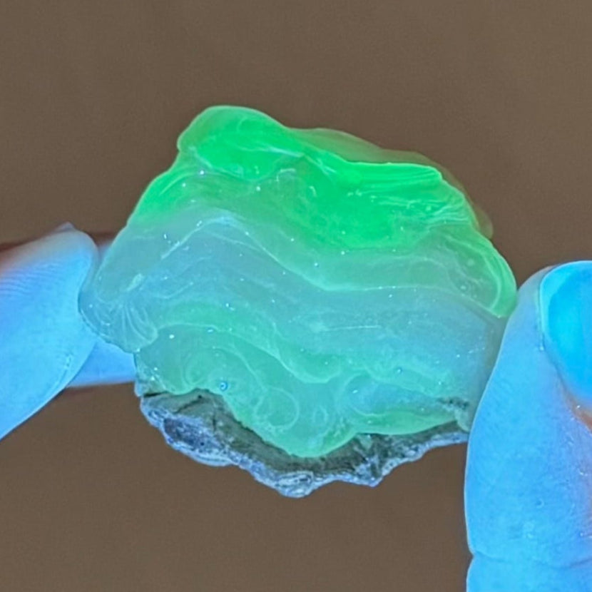 The specimen fluorescing strong yellow-green under UV light in low lighting. The upper layers stronger reaction than those in the middle that are milkier, and the base is green again.