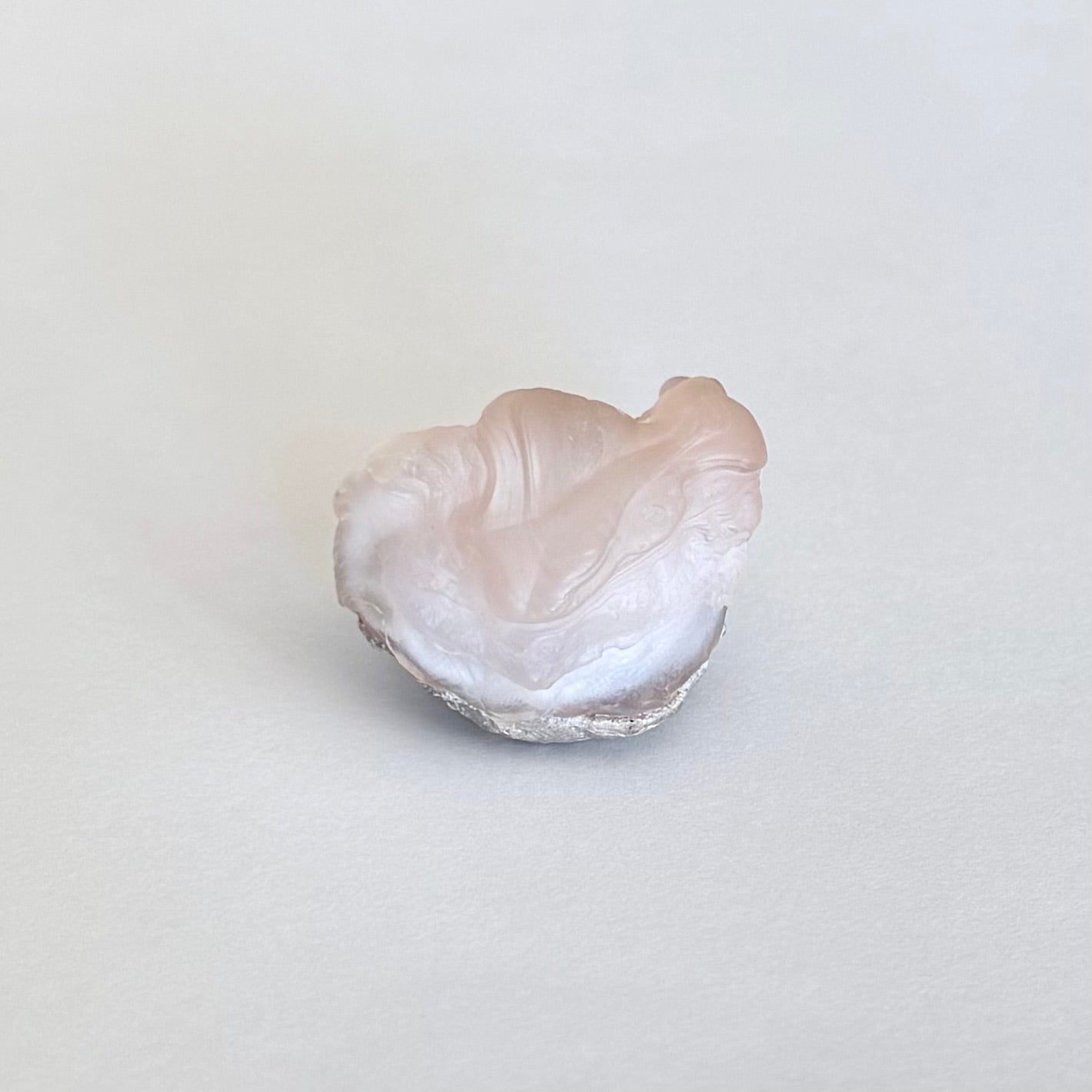 A more distant view of the specimen self-standing, showing the side with the bulbous pink formation and rippling layers below it.