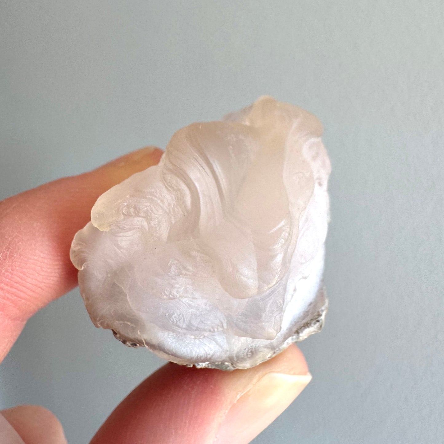 End-view of the specimen, a bulbous striated formation on the top with fluid flow as if dripping over the side of the piece.