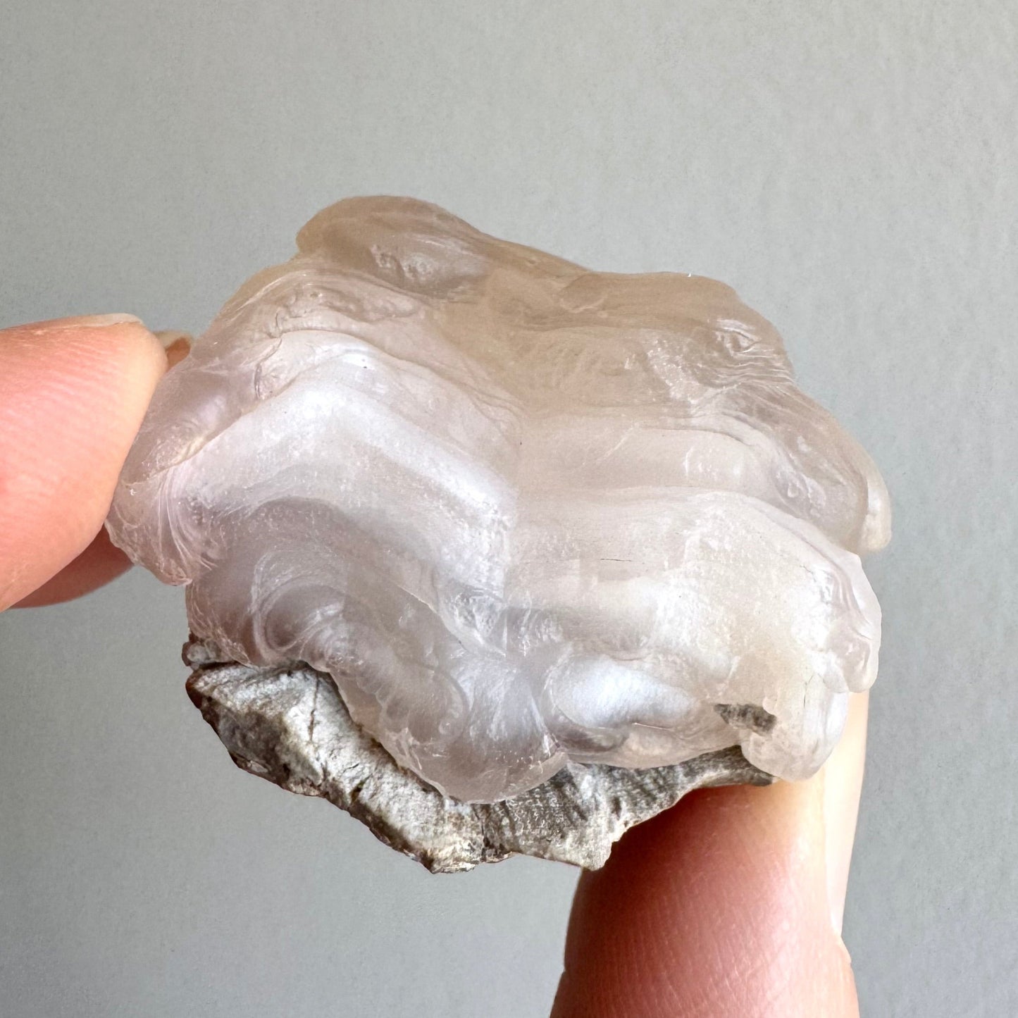 A pink chalcedony nodule with stacked thick ropy banding on a small piece of light gray matrix. The top and bottom layers have more translucency and a light pinkish coloration, and some undulating white layers are visible in the center.