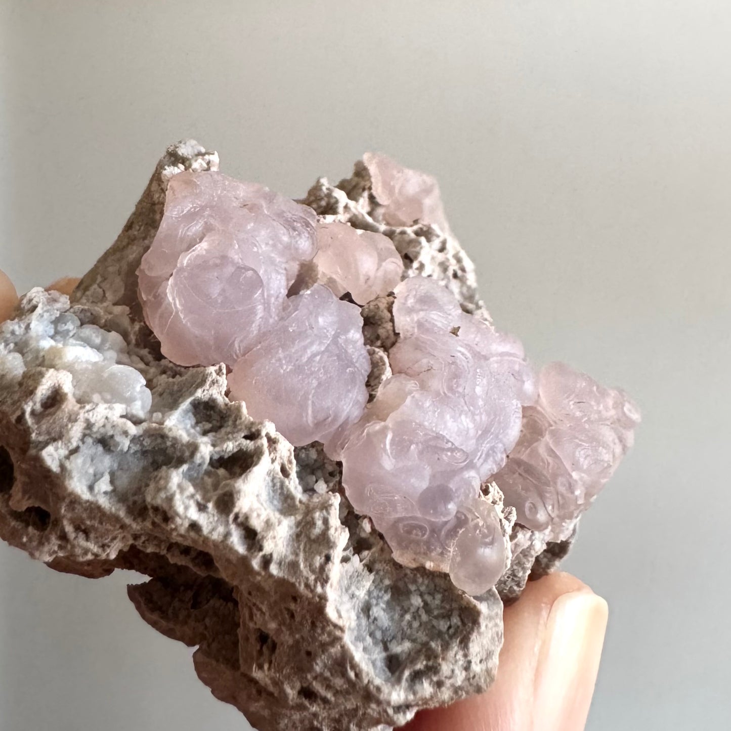 Detailed side-view of the piece, showing craggy volcanic texture to the matrix with small swirling botryoidal forms of chalcedony arranged fluidly on the surface. The chalcedony has ropy texture with some concentric banding.