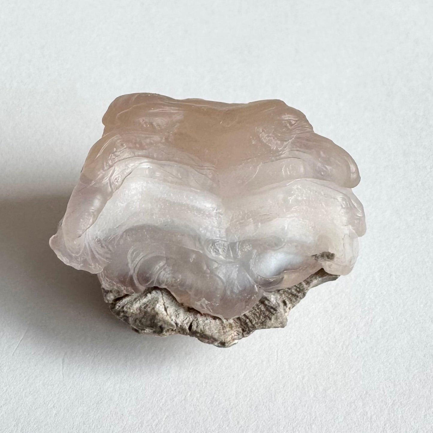 A close detail view of the side of the piece with this ropy layers stacked tall, with swirling botryoidal forms along the base where it attaches to the matrix.