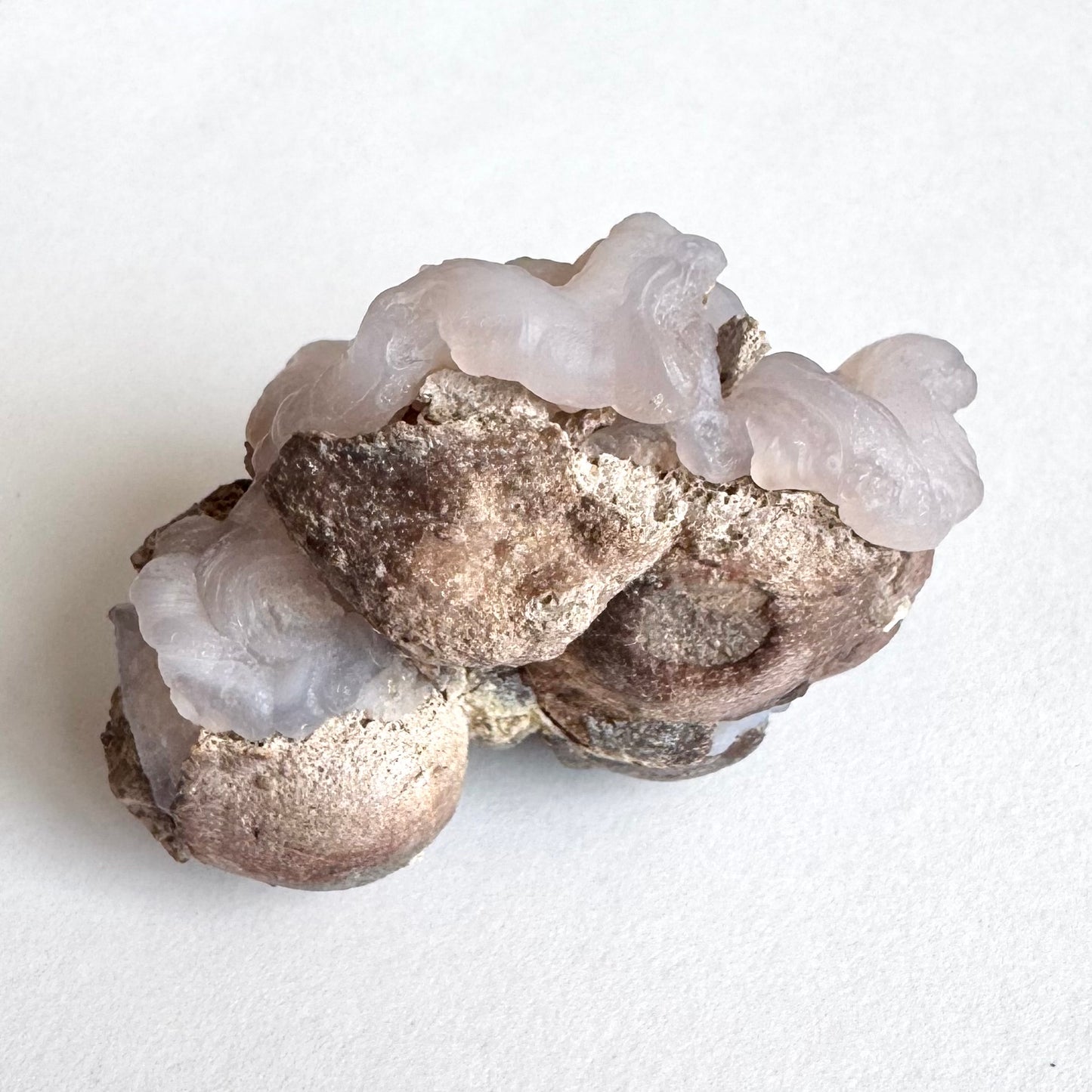 Side-view of the specimen, the chalcedony nodules backed with rounded cups of a brown rock matrix. The thick ropy chalcedony rims curl over the matrix edges like a fluid pouring over the edge.