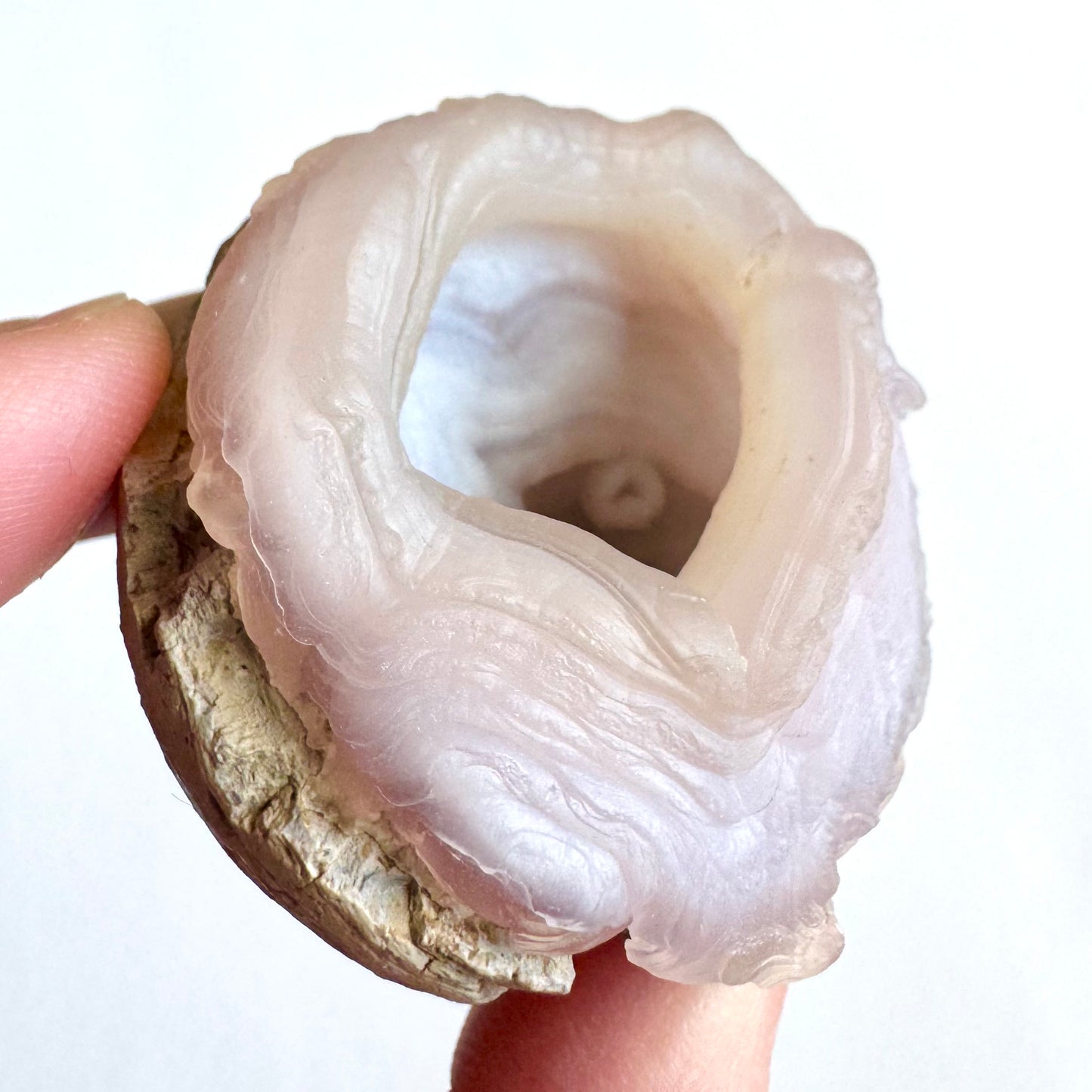Close angled view of the specimen, showing the subtle rosy pink color. The rim of the opening comes to a point, with flow-like pattern down the side. The small ring is visible inside, with agate banding around it.