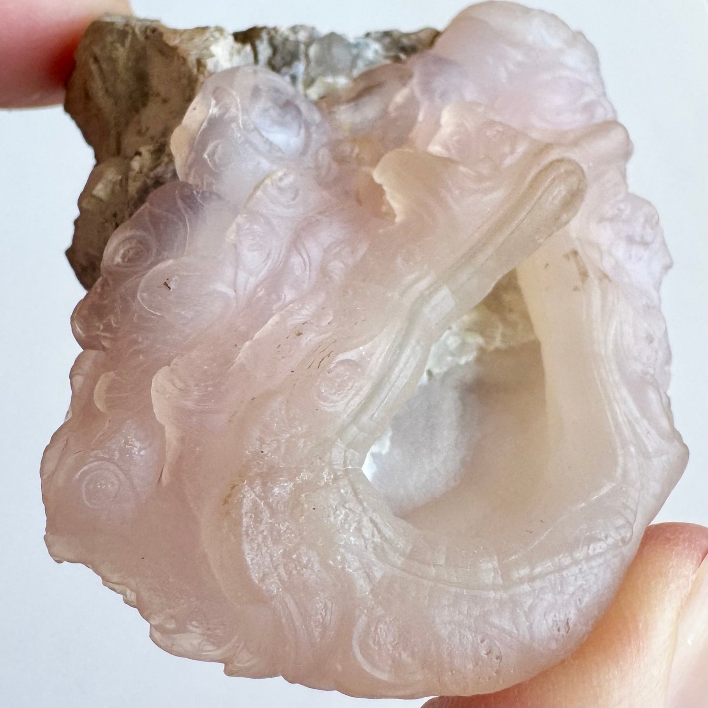 Close detail view of a side of the piece with quite a few small round botryoidal forms with rings of layers and slightly swirling pattern. The rim of the opening has distinct banding like lips.