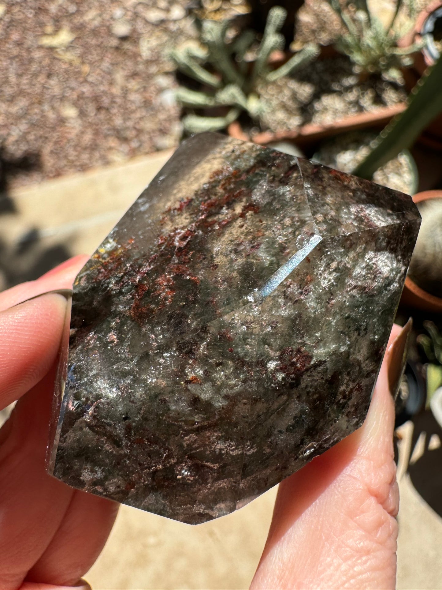 The piece held down with light shining on it, showing a thin beveled edge reflecting in the light. Chunky red and white chlorite and wispy green inclusions are visible