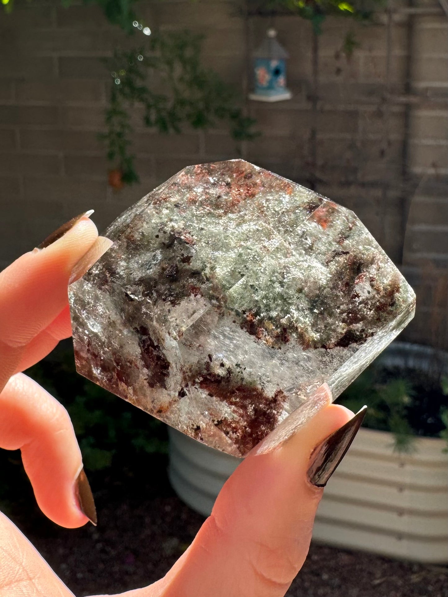 The garden quartz at another angle, with a sweeping curving line of dark red and green inclusions, with wispy inclusions illuminated by sunlight between them.