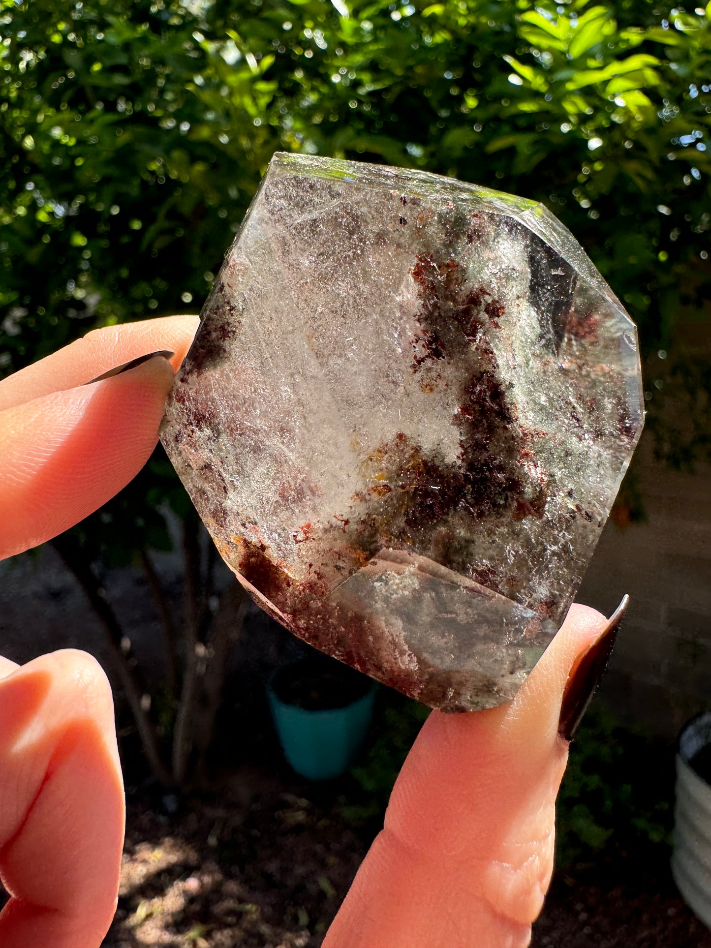 A marquise-shaped side of the piece, wide in the middle and pointed on the ends. It has good clarity through part on the right, but mostly is filled with wispy inclusions. There are also bunchy dark red-brown and yellow-brown inclusions that look like seaweed running through the center.