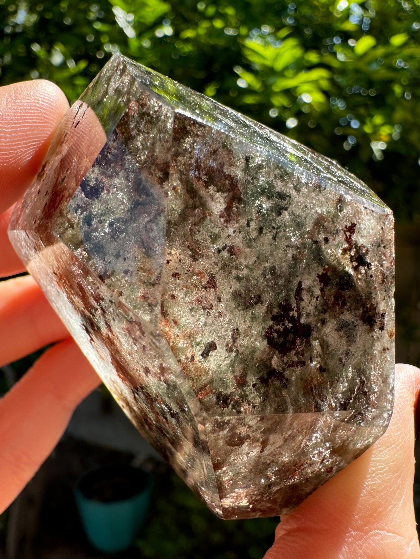 A side-view of the garden quartz held up in the sunlight, with wispy inclusions inside the quartz illuminated and dark brown chlorite spots.