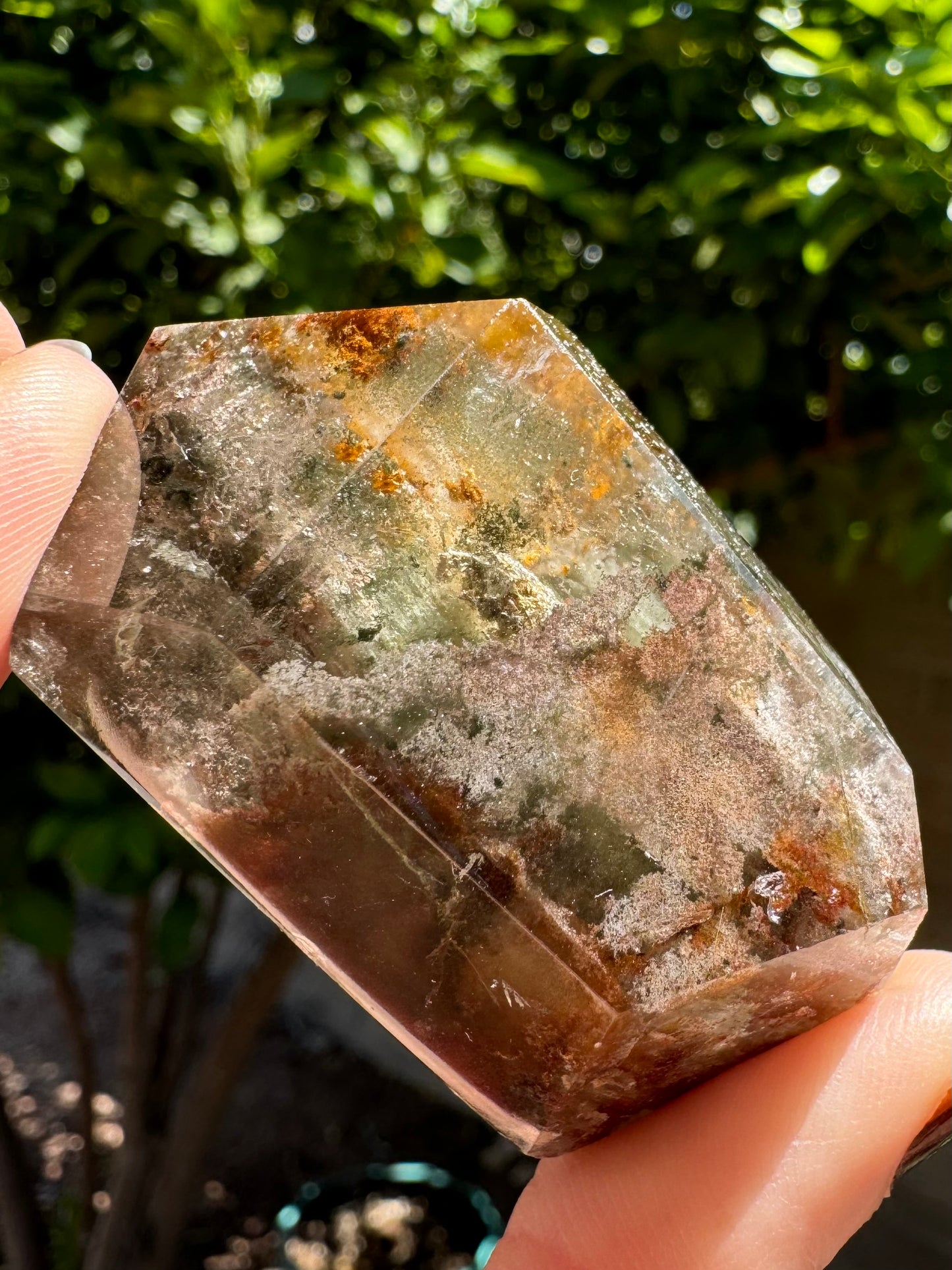 Piece of garden quartz with colorless, green, rusty orange-brown, and light off-purple inclusions, with pattern dark in the lower corner.