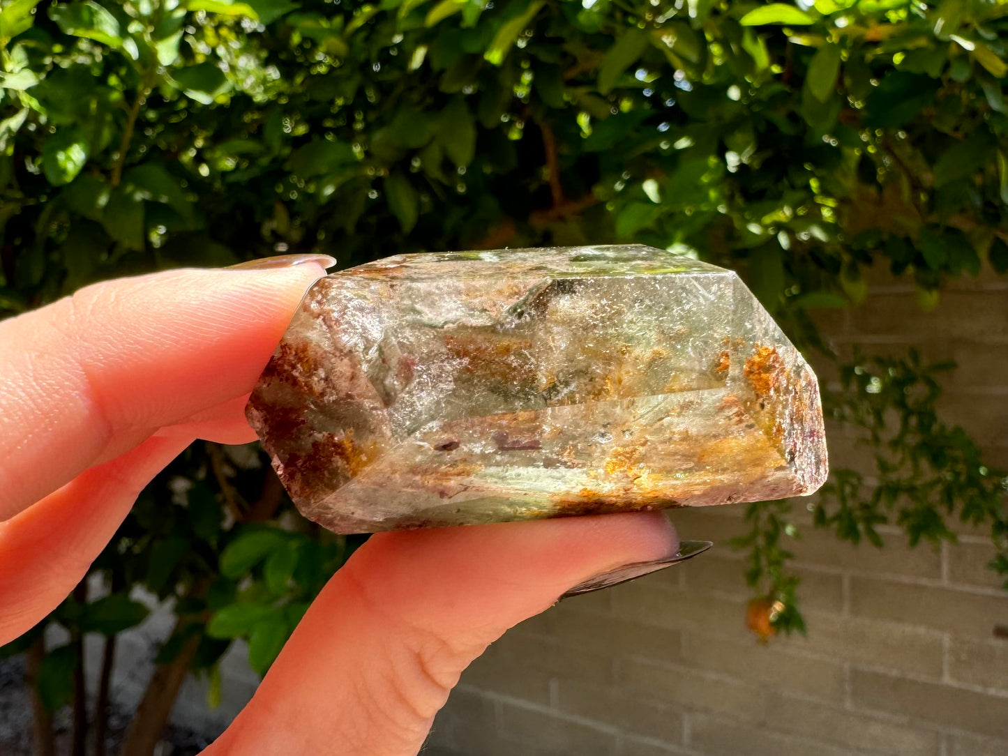 Side-view of the piece of garden quartz, with green and brown inclusions making the base semi-opaque, and wispy colorless inclusions lit up in the top