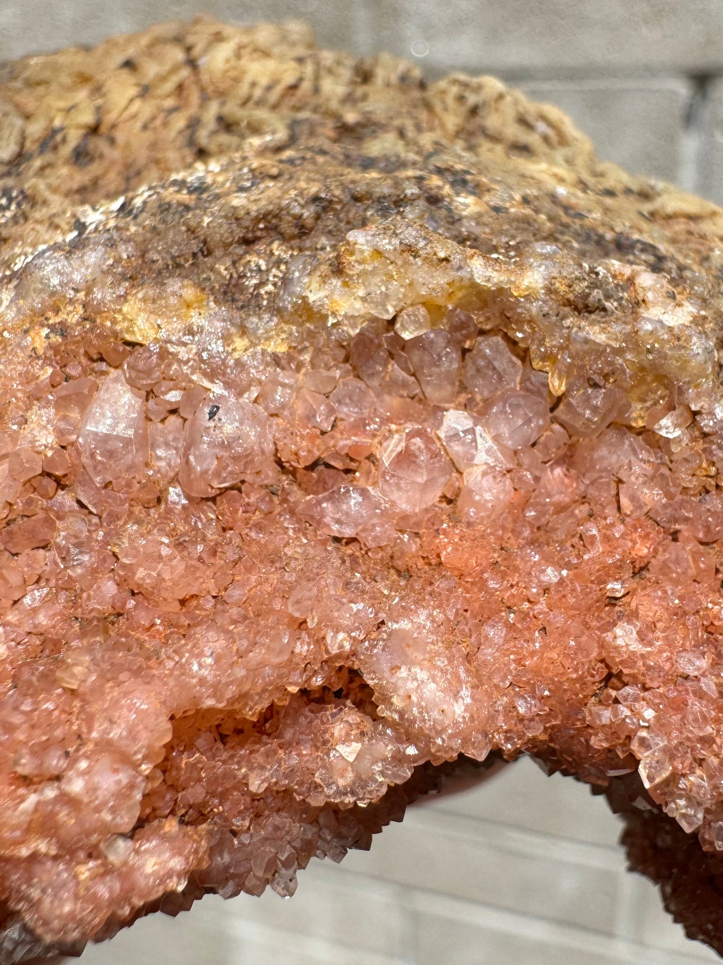Detail of an edge of the piece, showing larger colorless crystal grain sizes on the interior with smaller druzy growth included with hematite over it.