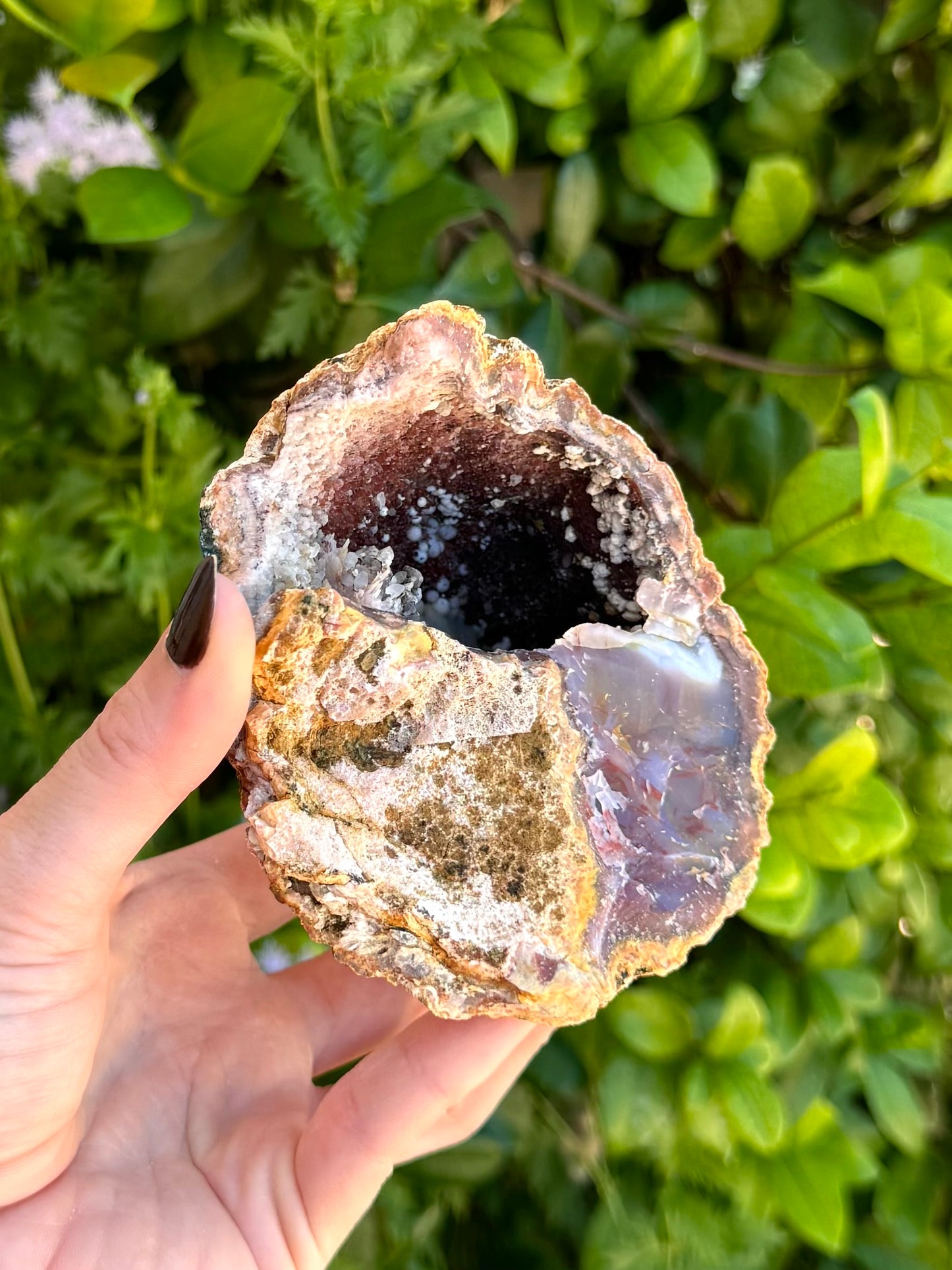Looking into the geode emphasizing to opposite wall, coated in dark red-brown chalcedony and spotted with white minerals.