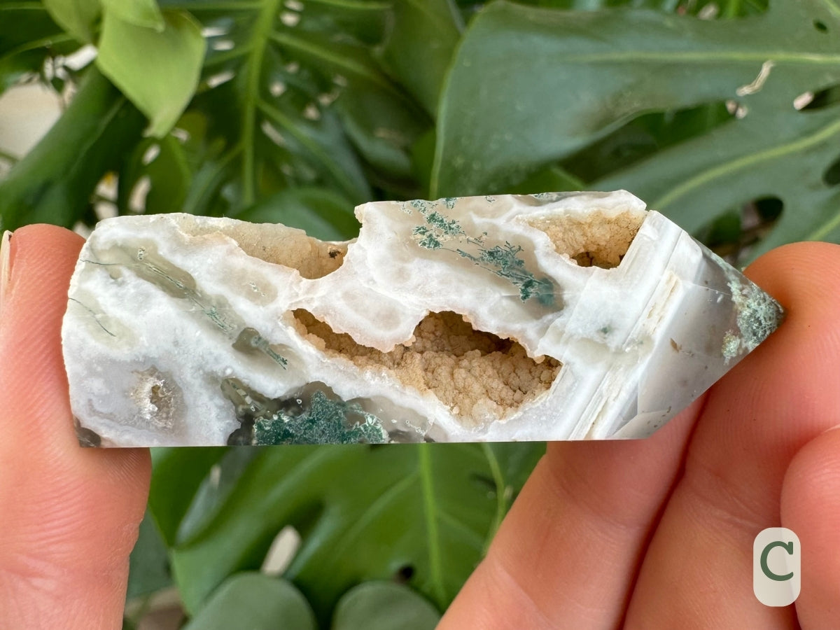 Option C, close view of a six-sided moss agate tower with large cavities and good pattern. It is white with translucent areas and some mossy blue-green inclusions. There is parallel striped white agate pattern near the tip.