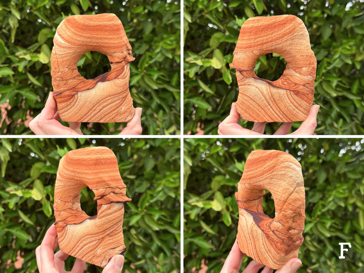 Option F, a blocky rounded rectangular shaped arch with a round hole through the center. The piece has vibrant red-orange color and very good pattern. Thin dark iron bands form curves and scallop patterns across the middle of the piece, forming ridges on the surface on each edge. Broad saturated layers curve across the top, and lighter higher contrast layers sweep across the bottom.