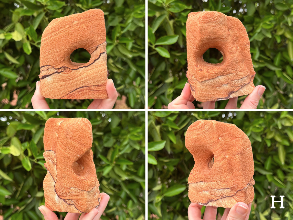Option H, a blocky squarish arch with rounded edges, three main wide faces and one thin edge. A round hole goes through the middle. Thin dark iron bands curve across the middle and base of the piece, the sandstone above red-orange with thin faint layering, and the highest point ringed with deeper orange-red layers. Below, the pattern is lighter with higher contrast.