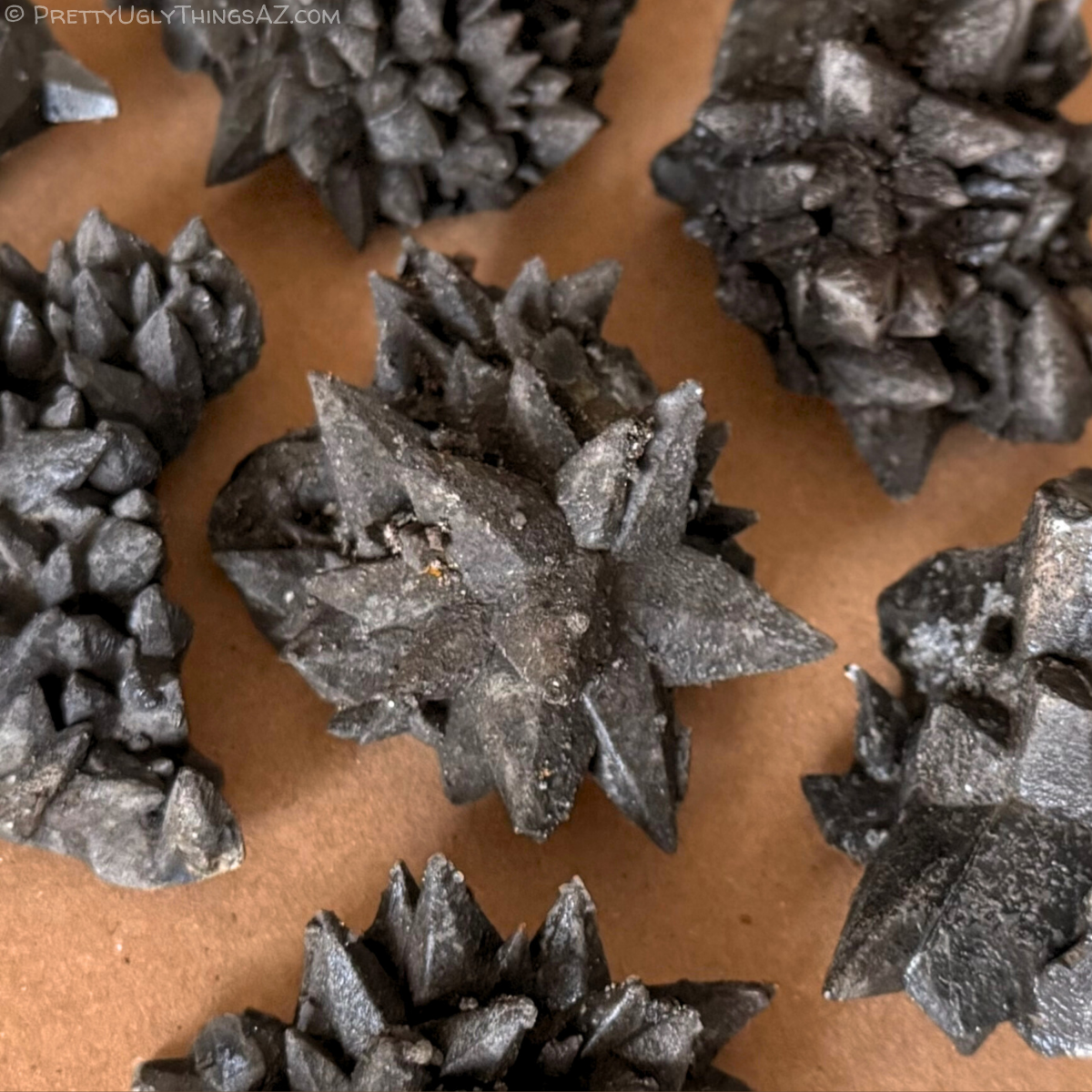 Several chocolate dogtooth calcite specimens spread on an orange-brown background. The minerals are opaque dark brown with large spiky crystals poking out in all directions. The surface is a rough texture, appearing matte and reflecting at the same time. Some small secondary crystals spot the specimens.