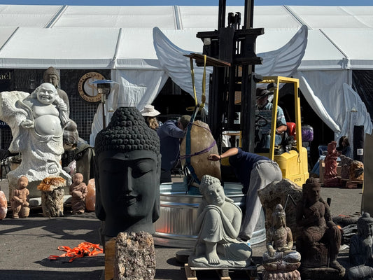Several people with a forklift, lowering smoky quartz point that is nearly as large as they are into around metal corral. There are large carved Buddha figures and minerals placed around the area.