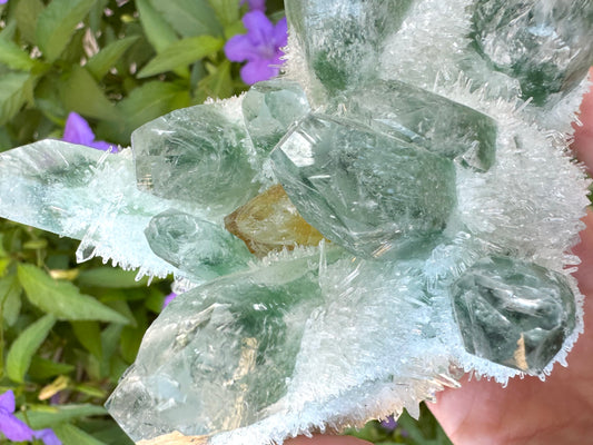 A green synthetic quartz cluster with one yellow crystal in the center, and a whitish crust of needle-like crystals