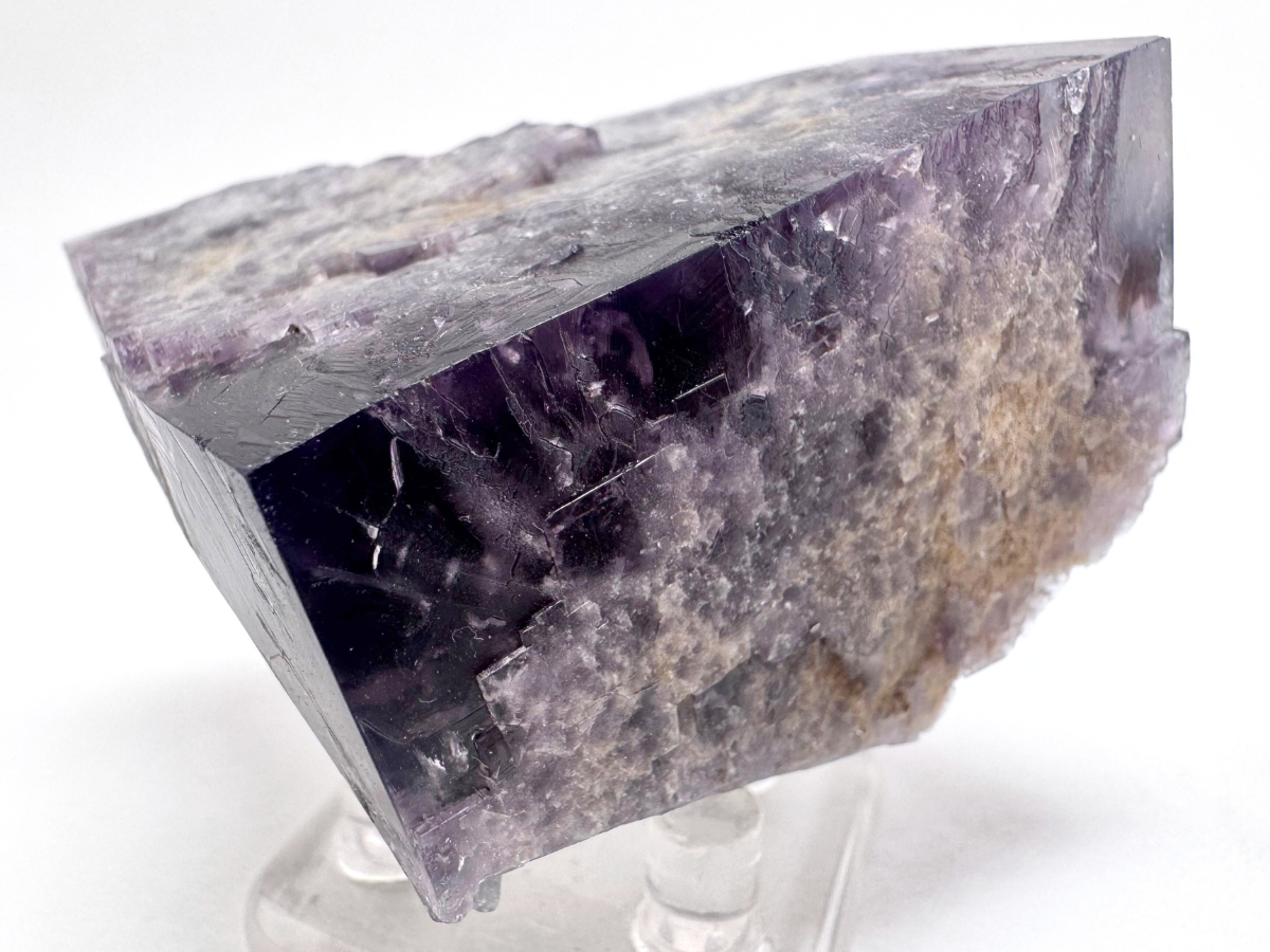 Detail view of a corner of the specimen, the interior inky dark. A band of concentrated purple color zoning near the surface. Square faces are arranged in a stepped pattern across the surface.