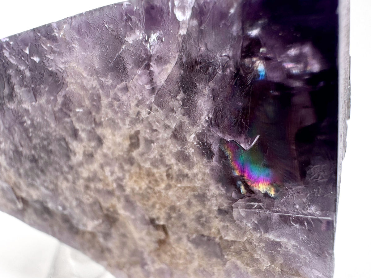 Close detail view inside one of the corners of the specimen, focused on a large rainbow flash of a natural fracture. There are faint diagonal cleavage lines etched into the surface.