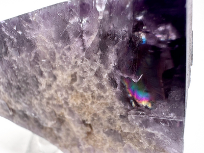 Close detail view inside one of the corners of the specimen, focused on a large rainbow flash of a natural fracture. There are faint diagonal cleavage lines etched into the surface.