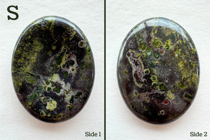 Option S, a grainy dark reddish gray base color with several colorful crystals embedded in it and seen in cross-section, with saturated green and blue green color and a ring of light lime around them. Some pocking on the back.