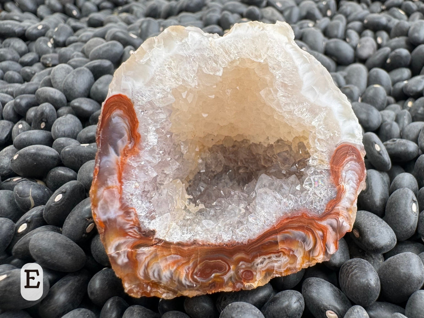 Option E: Detail of one half of the geode, the top half a creamy white and the bottom edge lined with rings of red-brown and white agate swirls. The darker outside can be seen through the druzy interior