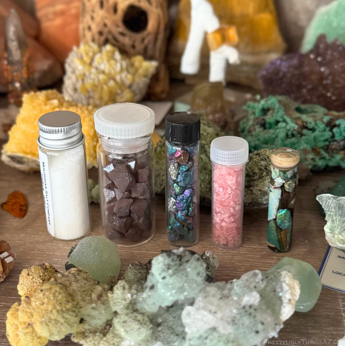 A row of five different vials of minerals on a mineral shelf, a vial of chalcopyrite in the center of the row.