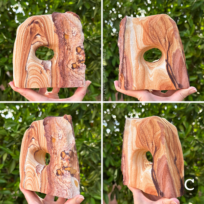 Option C, a blocky rounded off-square arch with an oval hole through the center. The piece has high-contrast pattern, with dark orange-brown layers looping across cream colored sandstone. One edge is near-white with splotchy dark purple-red iron pattern.  The other main face has simple, artistic orange, white, and dark purple pattern.