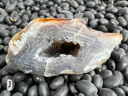 Option J: Detail of one of the geode halves, a dark semi-translucent chalcedony with swirls through it composed of white spots, with the spots aligned with solid straight lines on one side.