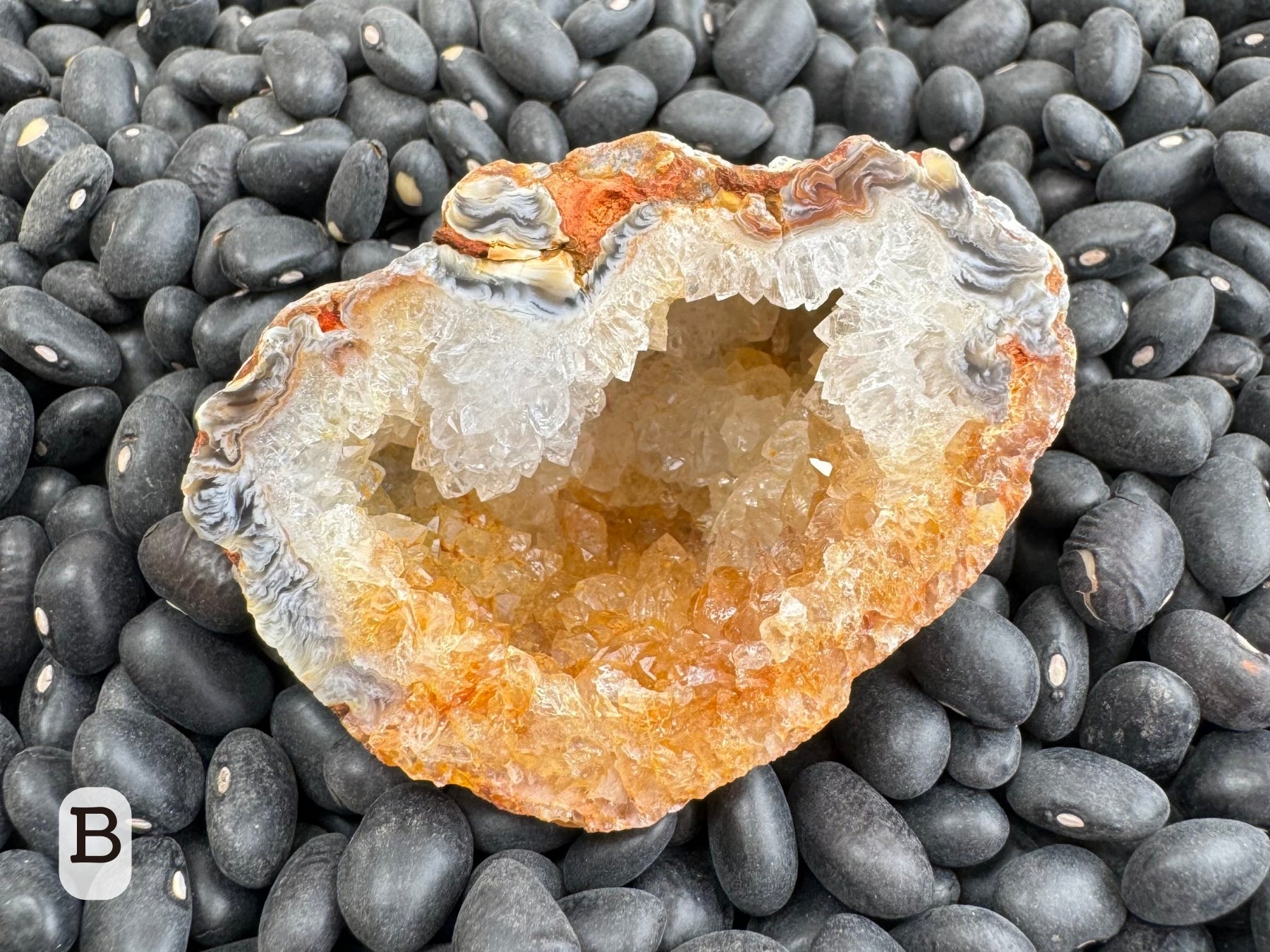 Option B: detail of one half of the geode, the top half colorless druzy and the bottom half stained orange. The edge has swirling black and white patterns with some vivid orange mixed in.